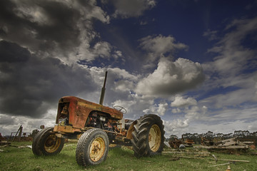 
Vintage tractor in field against a dynamic cloudy blue sky background
