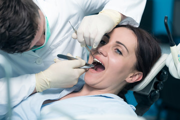 Fototapeta premium Dentist examining Patient teeth with a Mouth Mirror. Dentist is a Man, Patient is a Woman. Patient is Relaxed and not scared of Dentist.