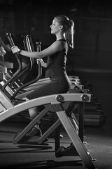 Fototapeta na wymiar Young woman at the gym exercising. Run on on a machine. Jogging workout in dark fitness club. Cardio. Black and white.