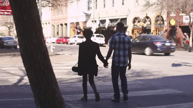 African American couple holding hands and walking across a city street