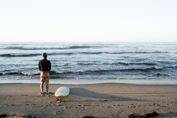 Male surfer evaluates the waves at sunrise in Long Island, New York