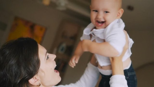 Young Happy Mother Holding her Newborn Child and throws up. Family at home. Beautiful smiling Mom and Happy Baby Together in bed.
