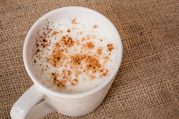 Hot beverage with cinnamon on sackcloth background