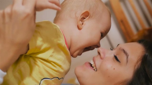Young Happy Mother Holding her Newborn Child and throws up. Family at home. Beautiful smiling Mom and Happy Baby Together in bed.