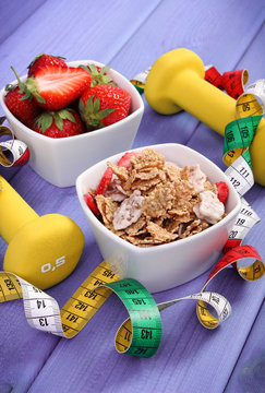 Fresh strawberries, wheat and rye flakes, dumbbells and centimeter, healthy and sporty lifestyle