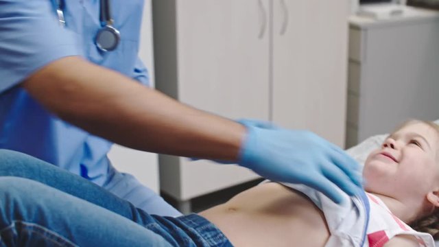 Tilt up of smiling doctor pressing on stomach of little girl and asking where it hurts