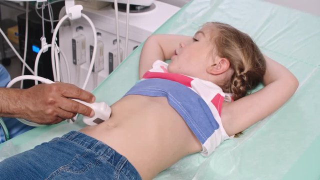 Hand of male doctor performing abdominal ultrasound on relaxed little girl