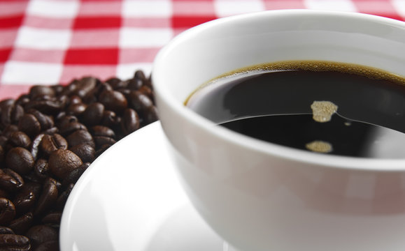 dark coffee in white cup with beans on the table and red tablecloth