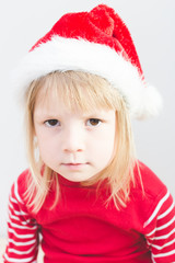 portrait of serious little blond girl wearing santa claus hat with big sad dark eyes