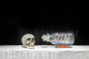 Human Skull with Ship in a Bottle with black background / Still life style