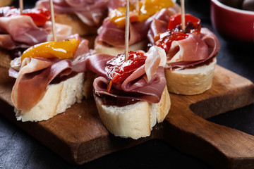 Spanish tapas with slices jamon serrano and grilled pepper. Also olives, salami, pickled onions, and peppers stuffed with cheese