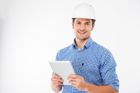 Cheerful Man Architect In Hard Hat Standing And Using Tablet