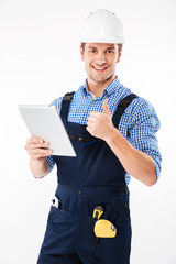Happy male builder showing thumb up and holding pc tablet