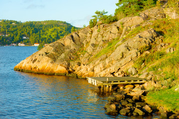 Evening sunshine on wooden pier on rocky shore. Saltbacken in Sweden, close to Norway (the houses and forest in the background).