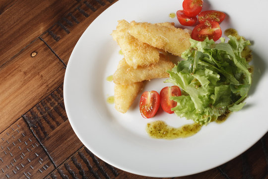 Breaded cheese (deep-fry) with tomatoes and greens in a white plate. Wooden background