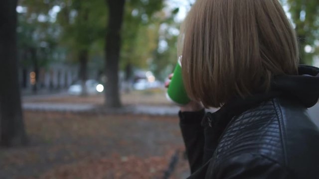 Young woman drinks coffee in the street at the evening