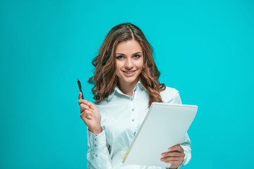 The smiling young business woman with pen and tablet for notes on blue background