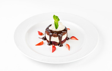 Dessert with chocolate sponge cake, vanilla cream, cherry, ice cream and strawberries on a plate on a white background
