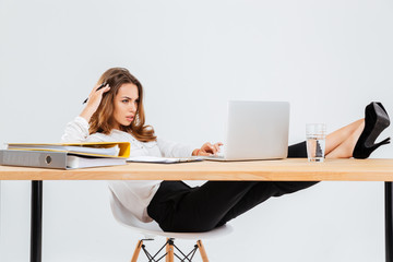 Pensive businesswoman using laptop and thinking with legs on table