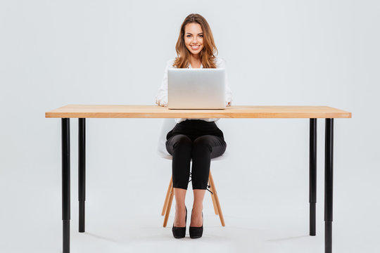 Attractive smiling businesswoman using laptop while sitting at office desk
