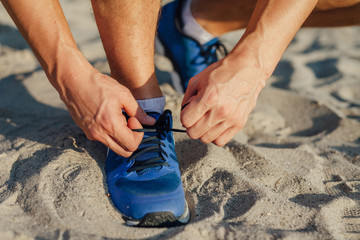 Man is tying shoelace while standing on the sand.