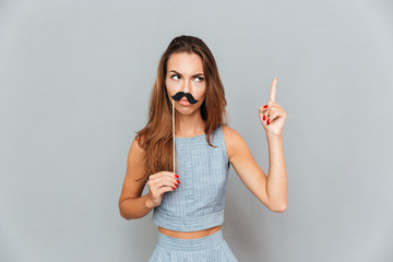 Serious amusing young woman with moustache props pointing up