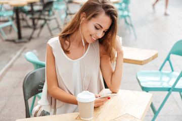 Woman with earphones listen music and typing message on smartphone