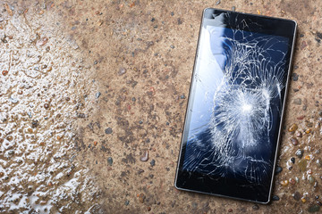 Broken Phone with cracked screen on wet concrete