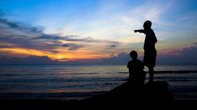 Man Teaching Boy, Silhouette on Beach During Colorful Island Sunset - 