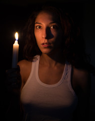 Mujer joven iluminada por la luz de una vela en una habitación completamente oscura tras un apagón - obrazy, fototapety, plakaty
