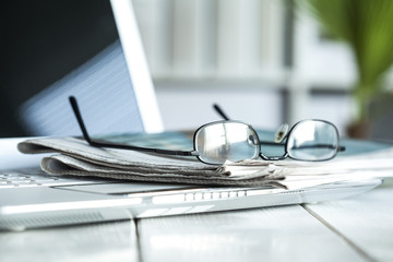 Stack of  newspaper with eyeglasses on laptop