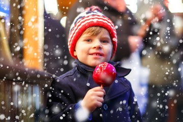 little kid boy eating sweet apple on Christmas market