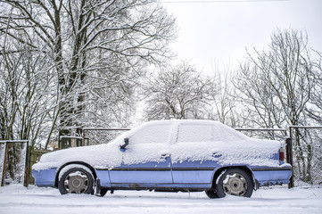 old rusty blue car covered with snow in winter