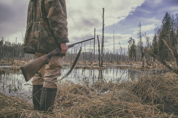 Hunter standing in the swamp in the forest and holding in his hand an old hunting rifle