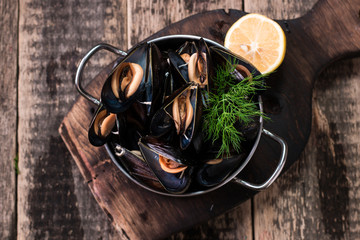 Mussels in copper cooking dish and lemon on dark wooden background