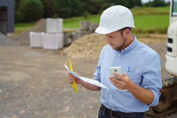 ernster handwerker mit bauplan und handy auf der baustelle