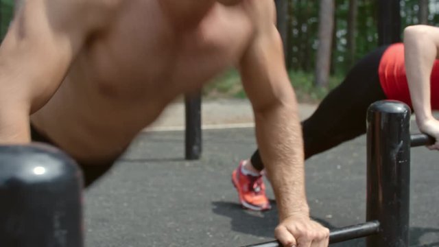 Sporty young woman and shirtless man doing push-ups on a bar in the park