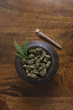 Cannabis sativa flower buds and leaf in wooden pot with rolled weed joint