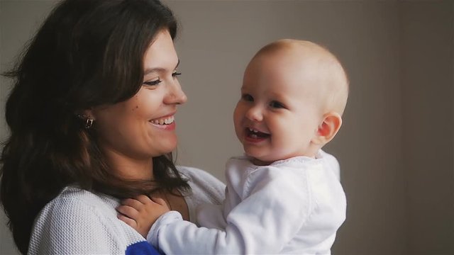 Young Happy Mother Holding her Newborn Child. Family at home. Beautiful smiling Mom and Happy Baby Together.