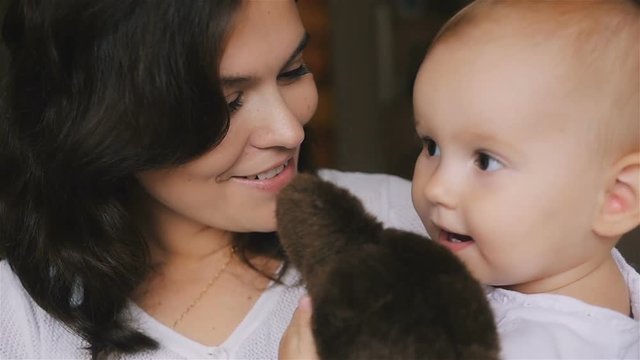 Young Happy Mother Holding her Newborn Child and kissing. Family at home. Beautiful smiling Mom and Happy Baby Together. Tenderness concept.