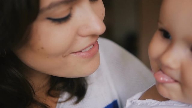 Young Happy Mother Holding her Newborn Child and kissing. Family at home. Beautiful smiling Mom and Happy Baby Together. Tenderness concept.