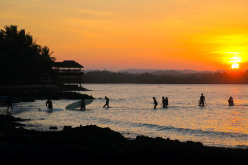 Surfers Walking Back to the Beach With their Surfboards, Orange Sunset Silhouette at Cloud 9 , Siargao Island - Philippines