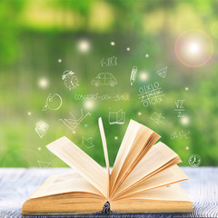 Book on wooden table. Icons on blurred green background. Knowledge concept.
