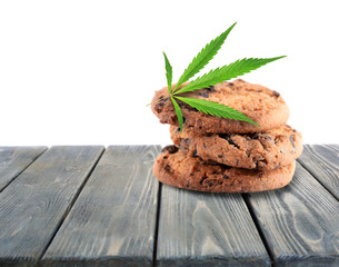 Tasty cookies with marijuana leaf on wooden table with white background