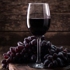 Glass of red wine, served with grapes on a wooden background