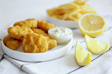 Tasty nuggets with sauce in plate and lemon on napkin
