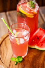 Watermelon lemonade with lemon and mint in a glass and a jug on