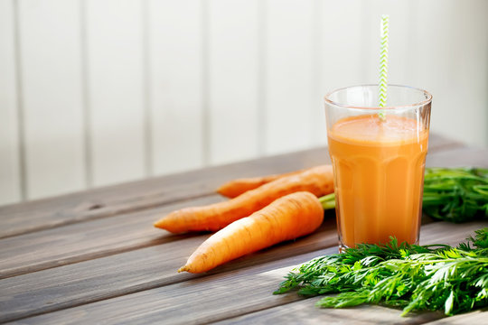 Carrot fresh juice in a glass and carrots with tops of vegetable