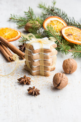 Obraz na płótnie Canvas Close up of homemade butter nuts star shaped cookies with icing, pine, orange slices,cinnamon, anise, walnuts and golden ribbon over white wood background. Christmas decoration.