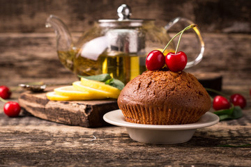 Tasty muffin with cherry and mint on vintage wooden background